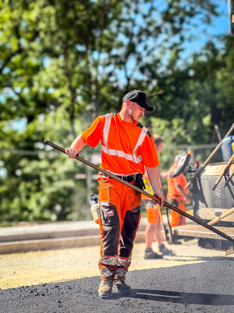 Straßenbauer verteilt frischen Asphalt mit Handwerkzeug auf der Baustelle