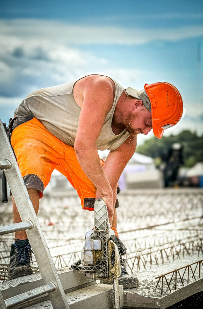 Person in Arbeitskleidung bearbeitet auf einer Baustelle mit einer Trennsäge ein Betonelement