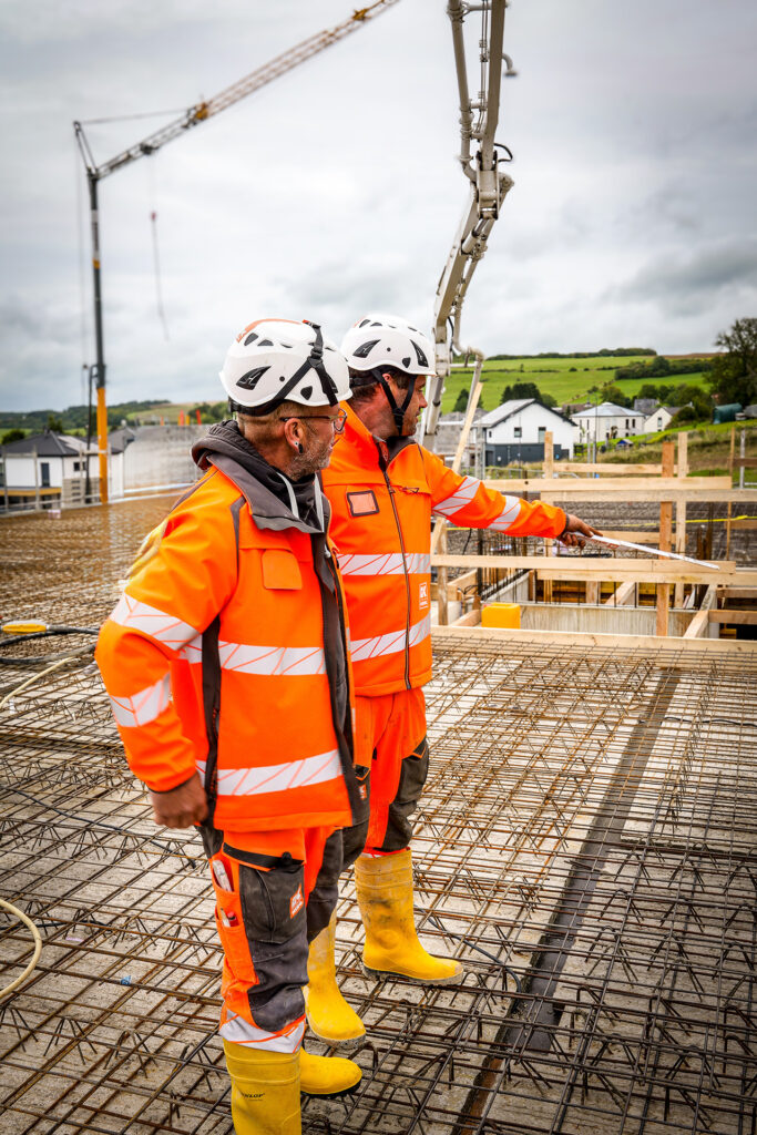 Zwei Mitarbeiter auf einer Baustelle stehen auf einer Bewehrung und besprechen den weiteren Arbeitsablauf