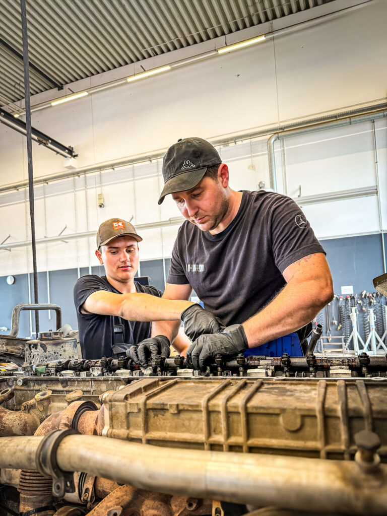 Zwei Mitarbeiter arbeiten gemeinsam an einem geöffneten Motor in einer Werkhalle